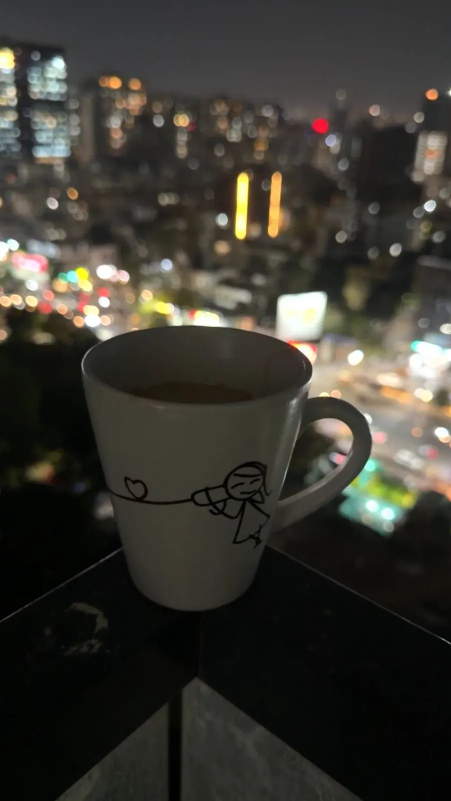 A cup of chai on a balcony rail with the Pune skyline out of focus behind it