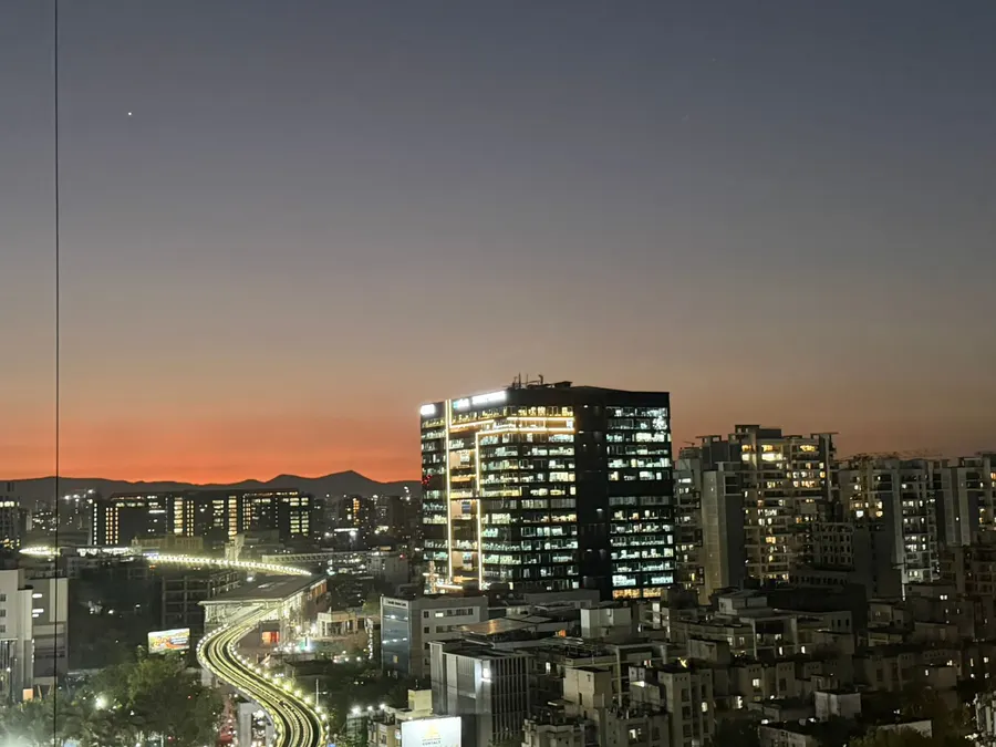 Pune skyline at dusk, orange horizon behind lit office towers